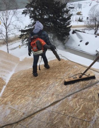 A man clearing snow off a roof using a snow blower.