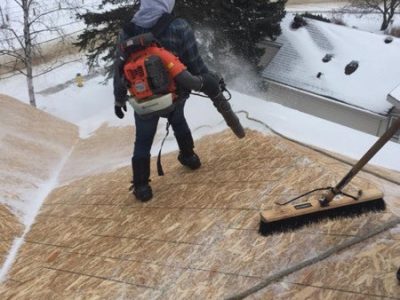 A man clearing snow off a roof using a snow blower.