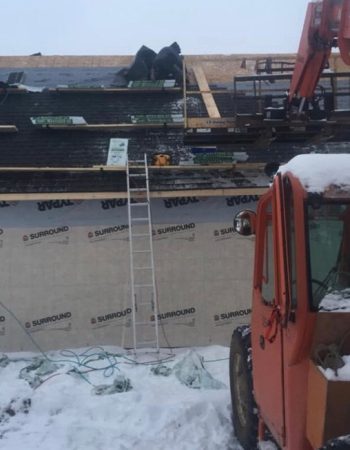 A construction worker repairing a roof covered in snow, wearing a hard hat and safety gear.