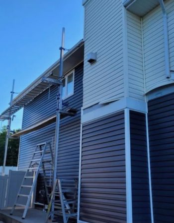 A house being painted with blue siding, a ladder leaning against the wall.